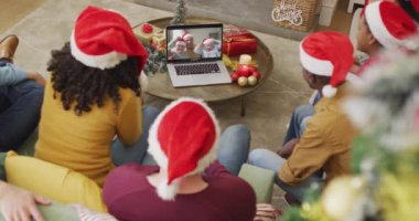 Noel Baba şapkalı çeşitli aileler, ekranda mutlu bir aileyle yılbaşı görüntülerinde dizüstü bilgisayar kullanıyorlar. Noel, şenlik ve iletişim teknolojisi.