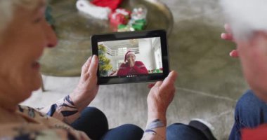 Gülümseyen Kafkasyalı çift, ekranda kadınla birlikte noel videosu için tablet kullanıyor. Noel, şenlik ve iletişim teknolojisi.