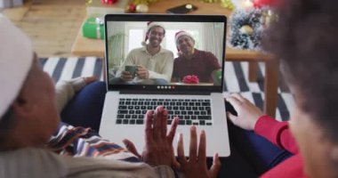 Afrika kökenli Amerikalı anne ve kız, ekranda ailesiyle birlikte yılbaşı görüntülü konuşma için dizüstü bilgisayar kullanıyorlar. Noel, şenlik ve iletişim teknolojisi.