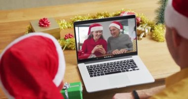 Noel Baba şapkalı beyaz bir baba ve oğul, ekranda aileleriyle yılbaşı görüntülerinde dizüstü bilgisayar kullanıyorlar. Noel, şenlik ve iletişim teknolojisi.