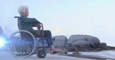 Sahilde denize bakan, tekerlekli sandalyeli, gülümseyen yaşlı, beyaz bir kadının üzerinde hareket eden ışığın canlandırması. emeklilik, ev hayatı ve umut kavramı dijital olarak oluşturulmuş animasyon.