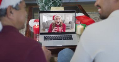 Gülümseyen bir çift ırklı baba ve oğul, ekranda bir kadınla yılbaşı görüntüsü için dizüstü bilgisayar kullanıyor. Noel, şenlik ve iletişim teknolojisi.