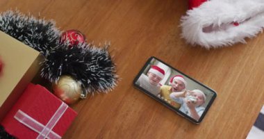 Noel 'de akıllı telefondan Noel Baba şapkası takan gülümseyen beyaz bir aile. Noel, şenlik ve iletişim teknolojisi.