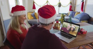 Noel Baba şapkalı, gülümseyen beyaz bir çift ekranda çiftle Noel 'de görüntülü konuşma yapmak için laptop kullanıyor. Noel, şenlik ve iletişim teknolojisi.