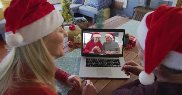 用笔记本电脑和家人一起在屏幕上进行圣诞视频通话 笑着带桑塔帽的高加索夫妇 圣诞节 节日和通信技术 — 图库视频影像
