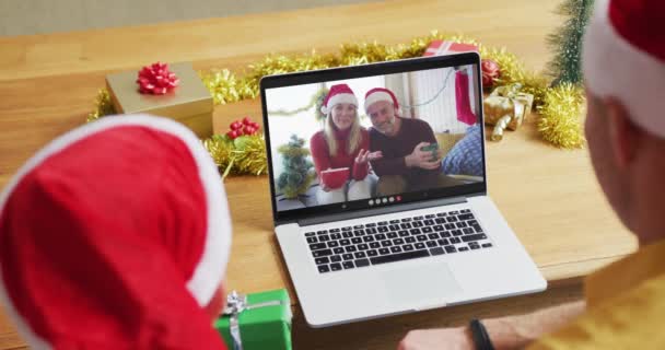 クリスマスのビデオ通話のためのラップトップを使用してサンタの帽子を持つ白人の父と息子は 画面上のカップルと クリスマスやお祭りや通信技術は — ストック動画