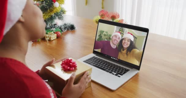 クリスマスのビデオ通話のためのラップトップを使用してサンタの帽子を持つアフリカ系アメリカ人女性は 画面上のカップルと クリスマスやお祭りや通信技術は — ストック動画