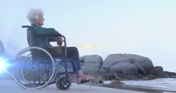 坐在轮椅上 面带微笑的资深高加索女人在海滩上望着大海 灯光的动画在她身上飘荡 家庭生活和希望概念数码动画 — 图库视频影像