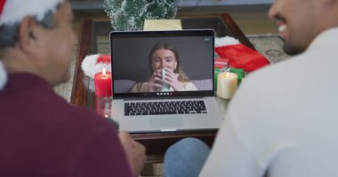 Gülümseyen bir çift ırklı baba ve oğul, ekranda bir kadınla yılbaşı görüntüsü için dizüstü bilgisayar kullanıyor. Noel, şenlik ve iletişim teknolojisi.