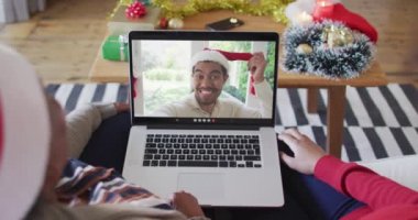 Afrika kökenli Amerikalı anne ve kız. Ekrandaki adamla yılbaşı videosu için dizüstü bilgisayar kullanıyorlar. Noel, şenlik ve iletişim teknolojisi.