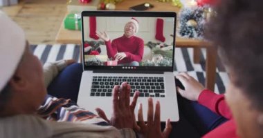 Afrika kökenli Amerikalı anne ve kız. Ekrandaki adamla yılbaşı videosu için dizüstü bilgisayar kullanıyorlar. Noel, şenlik ve iletişim teknolojisi.