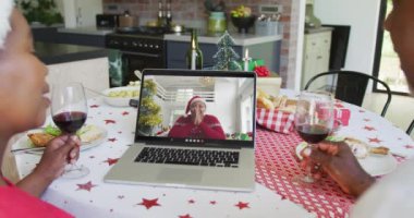 Şaraplı Afro-Amerikalı çift, dizüstü bilgisayarlarını ekranda bir kadınla yılbaşı görüntüsü için kullanıyorlar. Noel, şenlik ve iletişim teknolojisi.