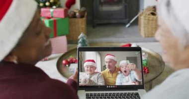 Birçok üst düzey bayan arkadaş, ekranda gülümseyen aile ile birlikte yılbaşı videosu için dizüstü bilgisayar kullanıyor. Noel, şenlik ve iletişim teknolojisi.