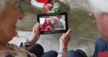 Gülümseyen Kafkasyalı son sınıf çifti, ekranda ailesiyle birlikte noel videosu için tablet kullanıyor. Noel, şenlik ve iletişim teknolojisi.