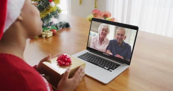 Africká americká žena se Santou klobouk pomocí notebooku pro vánoční video hovor s párem na obrazovce. Vánoční, slavnostní a komunikační technika.