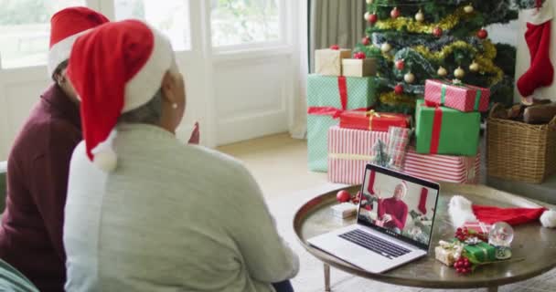 多様なシニア女性の友人は 画面上の男性とクリスマスビデオ通話のためのラップトップを振って使用しています クリスマスやお祭りや通信技術は — ストック動画
