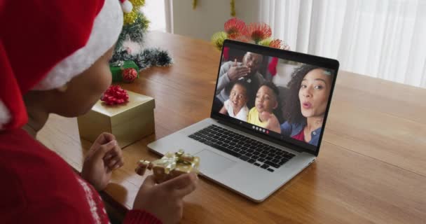 スクリーン上の家族とクリスマスのビデオ通話のためのラップトップを使用してサンタの帽子を持つアフリカ系アメリカ人女性 クリスマスやお祭りや通信技術は — ストック動画
