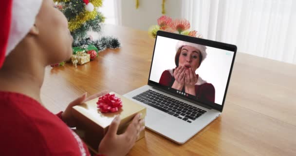 Afroamerikanerin mit Weihnachtsmütze mit Laptop für Weihnachts-Videoanruf mit Frau auf dem Bildschirm. Weihnachten, Fest und Kommunikationstechnologie.