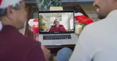Noel Baba şapkalı iki ırklı baba ve oğul, ekranda bir kadınla yılbaşı görüntüsü için dizüstü bilgisayar kullanıyorlar. Noel, şenlik ve iletişim teknolojisi.