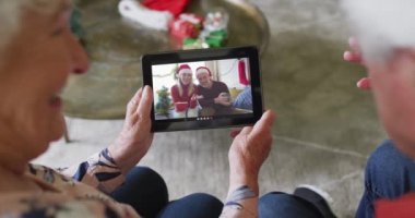 Gülümseyen Kafkasyalı çift, ekranda bir çiftle yılbaşı videosu için tablet kullanıyor. Noel, şenlik ve iletişim teknolojisi.