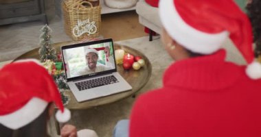 Noel Baba şapkalı çok yönlü aile, ekranda mutlu bir adamla yılbaşı görüntüsü için dizüstü bilgisayar kullanıyor. Noel, şenlik ve iletişim teknolojisi.