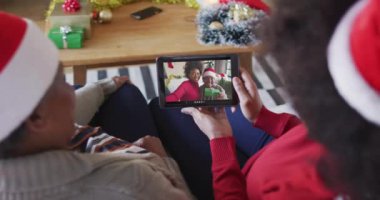 Afrika kökenli Amerikalı anne ve kız. Ekranda aileleriyle birlikte yılbaşı videosu için tablet kullanıyorlar. Noel, şenlik ve iletişim teknolojisi.