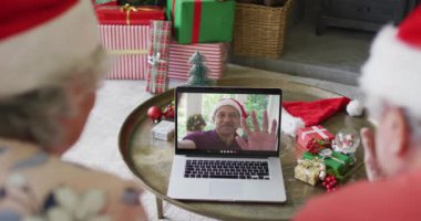 Noel Baba şapkalı Kafkasyalı çift ekrandaki adamla yılbaşı görüntüsü için laptop kullanıyor. Noel, şenlik ve iletişim teknolojisi.