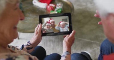 Gülümseyen Kafkasyalı son sınıf çifti, ekranda ailesiyle birlikte noel videosu için tablet kullanıyor. Noel, şenlik ve iletişim teknolojisi.