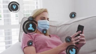 Evdeki akıllı telefonu kullanarak beyaz maskeli beyaz kadın üzerindeki dijital simgelerin canlandırılması. covid 19 pandemik konsept sırasında dijital olarak oluşturulan iletişim ve sosyal medya.