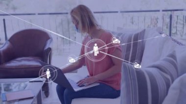 Bilgisayarı kullanarak, yüz maskesi takan beyaz bir kadının medya simgelerinin animasyonu. covid 19 salgın konsepti dijital olarak oluşturulurken küresel iş, bağlantılar ve dijital arayüz.