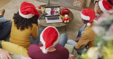 Noel Baba şapkalı çeşitli aileler, ekranda mutlu bir kadınla yılbaşı görüntüsü için laptop kullanıyorlar. Noel, şenlik ve iletişim teknolojisi.