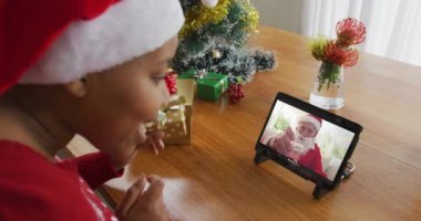 Noel Baba şapkalı Afrikalı Amerikalı bir kadın Noel Baba 'yı ekranda görmek için tablet kullanıyor. Noel, şenlik ve iletişim teknolojisi.