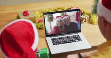 Noel Baba şapkalı beyaz bir baba ve oğul. Ekranda bir çiftle yılbaşı görüntüsü için dizüstü bilgisayar kullanıyorlar. Noel, şenlik ve iletişim teknolojisi.