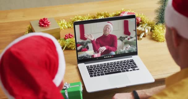 スクリーン上の男とクリスマスのビデオ通話のためのラップトップを使用してサンタの帽子を持つ白人の父と息子 クリスマスやお祭りや通信技術は — ストック動画