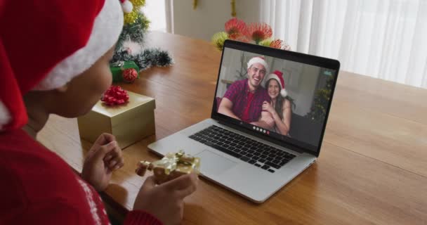 戴桑塔帽的非洲裔美国女人用笔记本电脑给屏幕上有夫妻的圣诞视频打电话 圣诞节 节日和通信技术 — 图库视频影像