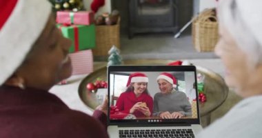 Gülümseyen çeşitli son sınıf kız arkadaşları ekranda aileleriyle birlikte yılbaşı videosu için dizüstü bilgisayar kullanıyorlar. Noel, şenlik ve iletişim teknolojisi.
