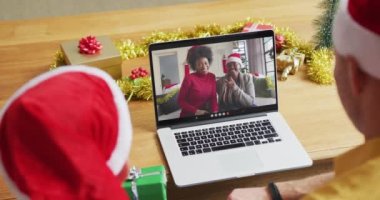 Noel Baba şapkalı beyaz bir baba ve oğul, ekranda aileleriyle yılbaşı görüntülerinde dizüstü bilgisayar kullanıyorlar. Noel, şenlik ve iletişim teknolojisi.
