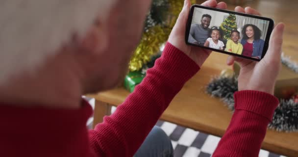 画面上の笑顔の家族とクリスマスのビデオ通話のためのスマートフォンを使用してサンタの帽子を持つ白人男性 クリスマスやお祭りや通信技術は — ストック動画