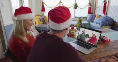 Noel Baba şapkalı, gülümseyen beyaz bir çift ekranda aileleriyle yılbaşı görüntüsü için dizüstü bilgisayar kullanıyor. Noel, şenlik ve iletişim teknolojisi.
