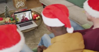 Noel Baba şapkalı çeşitli aileler, ekranda mutlu bir kadınla yılbaşı görüntüsü için laptop kullanıyorlar. Noel, şenlik ve iletişim teknolojisi.