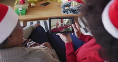 Afrika kökenli Amerikalı anne ve kız. Ekranda bir adamla noel videosu için tablet kullanıyorlar. Noel, şenlik ve iletişim teknolojisi.
