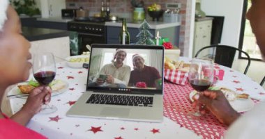 Şaraplı Afro-Amerikalı çift, mutlu bir aileyle yılbaşı görüntüsü için dizüstü bilgisayar kullanıyor. Noel, şenlik ve iletişim teknolojisi.