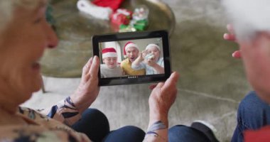 Üst düzey Kafkasyalı çift, mutlu bir aileyle Noel videosu için tablet kullanıyor. Noel, şenlik ve iletişim teknolojisi.