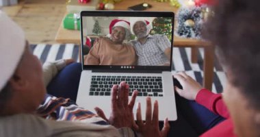 Afrika kökenli Amerikalı anne ve kız. Ekrandaki çiftle yılbaşı videosu için dizüstü bilgisayar kullanıyorlar. Noel, şenlik ve iletişim teknolojisi.