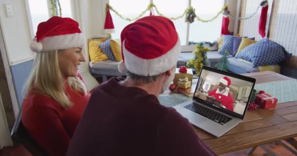 画面上のサンタとクリスマスのビデオ通話のためのラップトップを使用してサンタの帽子と笑顔白人カップル クリスマスやお祭りや通信技術は — ストック動画
