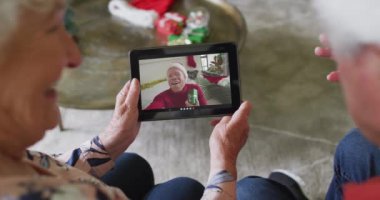 Üst düzey Kafkasyalı çift, ekranda mutlu bir adamla Noel videosu için tablet kullanıyor. Noel, şenlik ve iletişim teknolojisi.