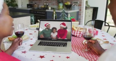 Şaraplı Afro-Amerikalı çift, mutlu bir aileyle yılbaşı görüntüsü için dizüstü bilgisayar kullanıyor. Noel, şenlik ve iletişim teknolojisi.