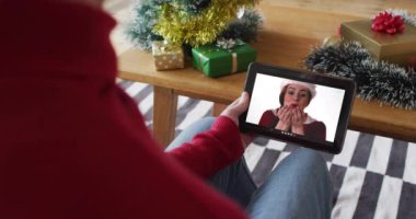 Beyaz bir adam ekranda gülümseyen bir kadınla yılbaşı videosu için el sallıyor ve tablet kullanıyor. Noel, şenlik ve iletişim teknolojisi.