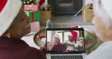 Farklı son sınıf kız arkadaşları, ekranda mutlu bir aileyle yılbaşı videosu için dizüstü bilgisayar kullanıyor. Noel, şenlik ve iletişim teknolojisi.