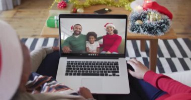 Afrika kökenli Amerikalı anne ve kız, ekranda ailesiyle birlikte yılbaşı görüntülü konuşma için dizüstü bilgisayar kullanıyorlar. Noel, şenlik ve iletişim teknolojisi.